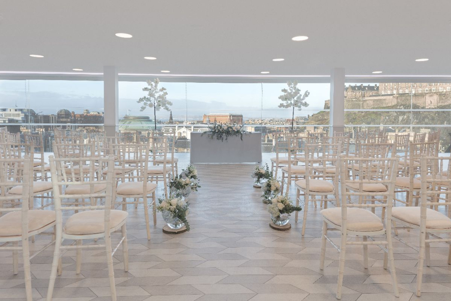 Ceremony set up in the SKYBar with views across Edinburgh, featuring white chiavari chairs and other white decor